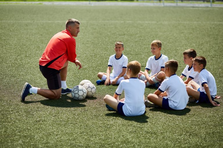 Entraîneur de football donnant des consignes à un groupe de jeunes joueurs lors d'un stage sportif Sport'n Go